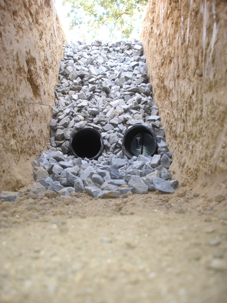 Twee drainagebuizen tussen grind in een uitgegraven sleuf